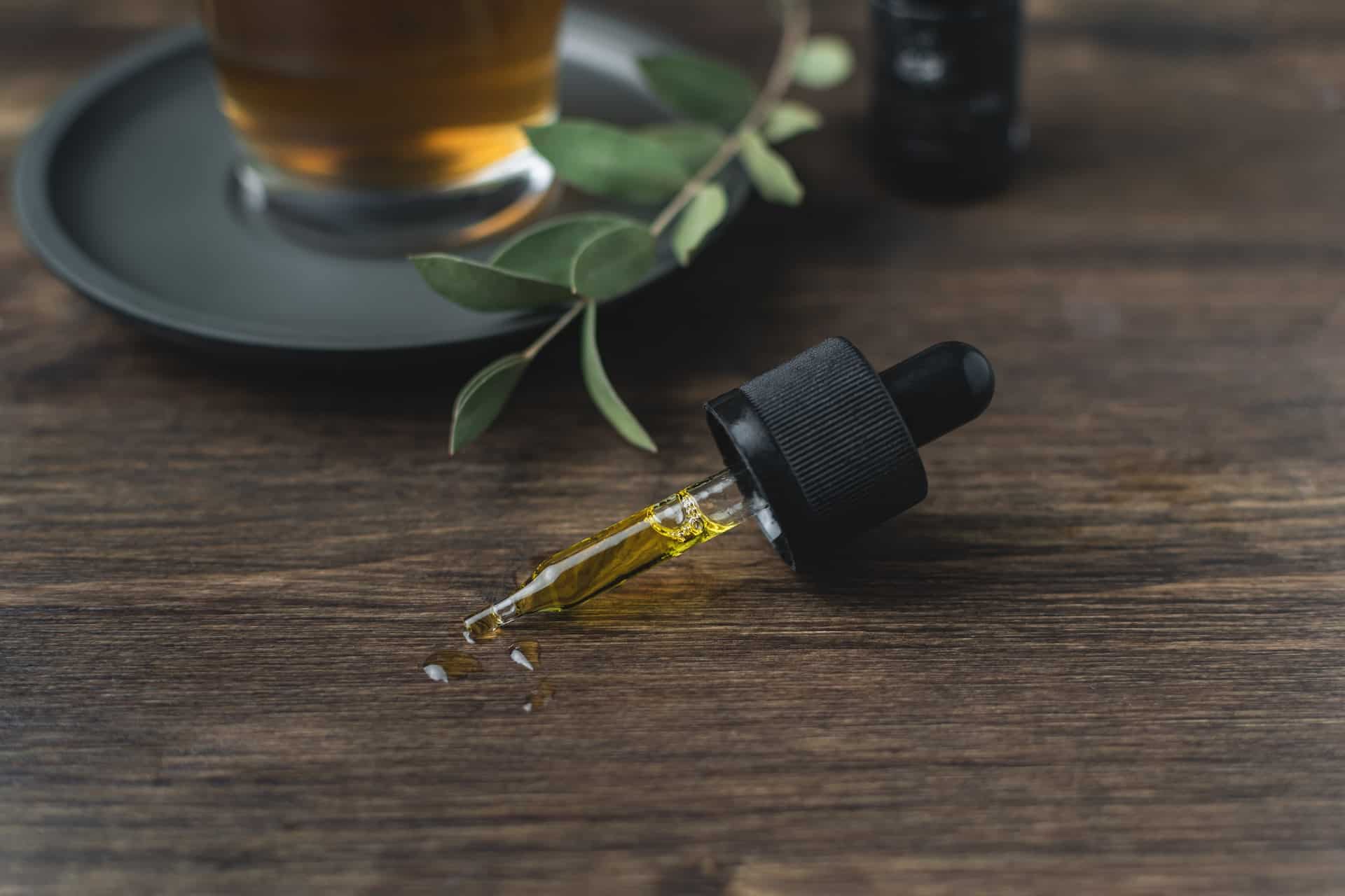 Dropper of CBD oil on a table with a plant stem